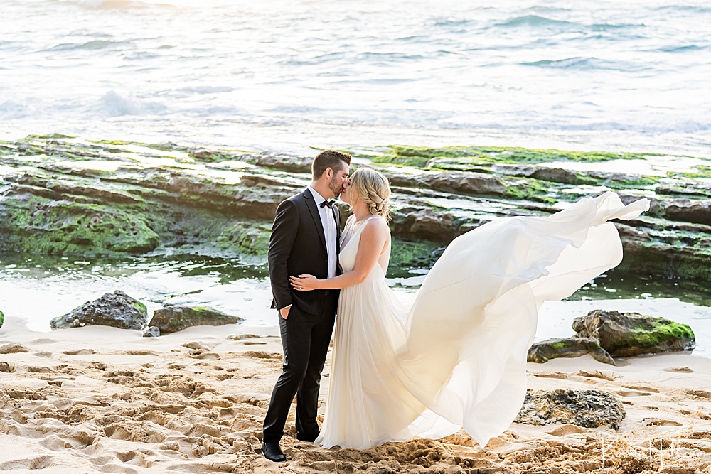 bride and groom kissing on beach while her dress blows in the wind in Hawaii 