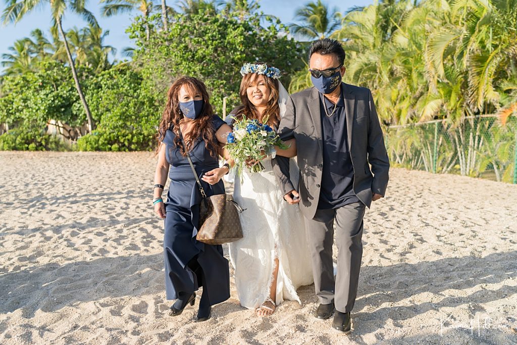 bride is escorted by parents wearing covid masks during a beach wedding in oahu 