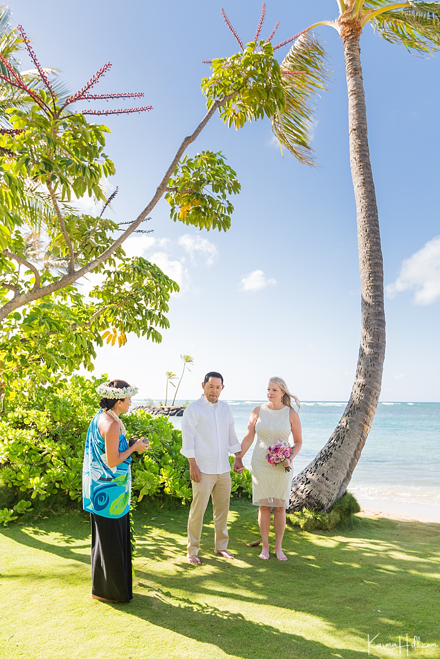 couple stands beneath a palm tree with ocean in the background as they marry in oahu 